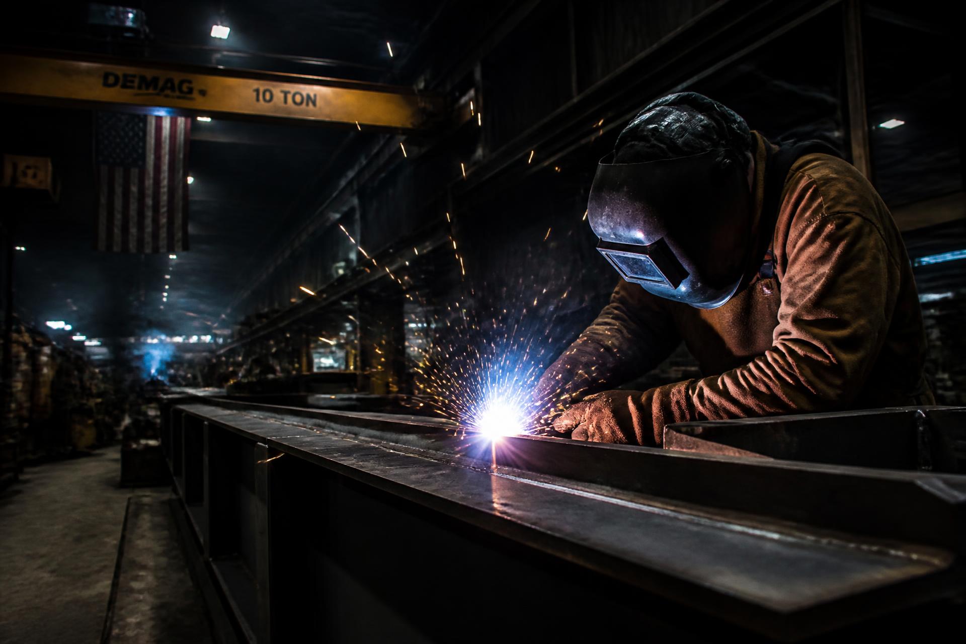 Welder shaping a steel beam under a shower of sparks in the WeldingGiants workshop